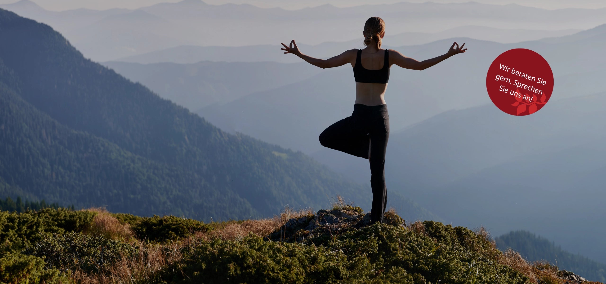Frau in Yoga-Pose auf einem Berg mit weitem Blick ins Tal