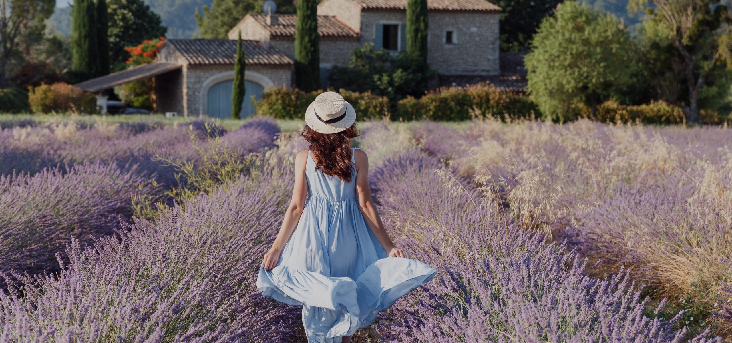 Frau im Sommerkleid geht durch ein blühendes Lavendelfeld in der Provence – Symbol für natürliche Ruhe, Entspannung und ganzheitliches Wohlbefinden.